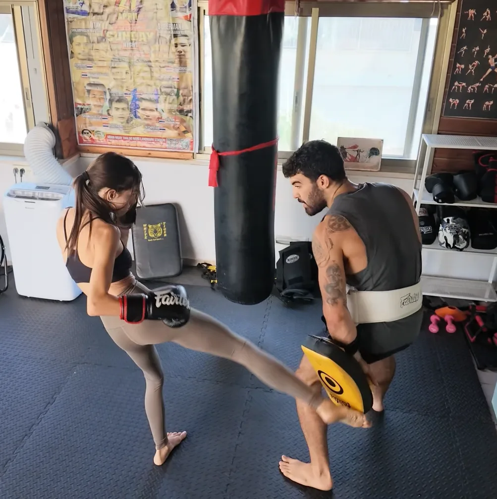 מתאמנת בועטת בעיטה מעגלית אל פד שאיתי לוי מחזיק, באימון אישי